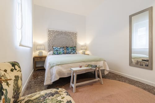 Bright bedroom at G&H Apartments in Jerez with queen bed, patterned headboard, blue pillows, wooden nightstands, table bench,