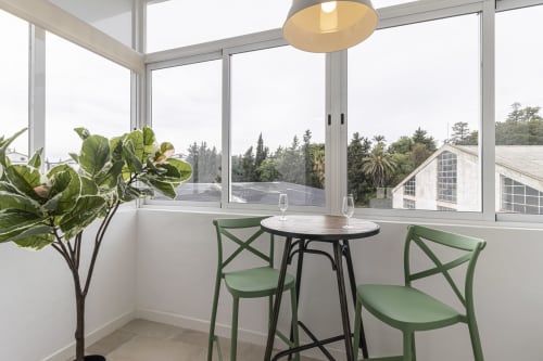 Modern apartment dining area with green chairs, round table, and panoramic windows overlooking Jerez vineyards at G&H