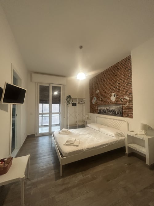 Camera moderna della B&B Gate 10 Bologna con letto bianco, muro in laterizio a vista, TV a schermo piatto e accesso al balcone