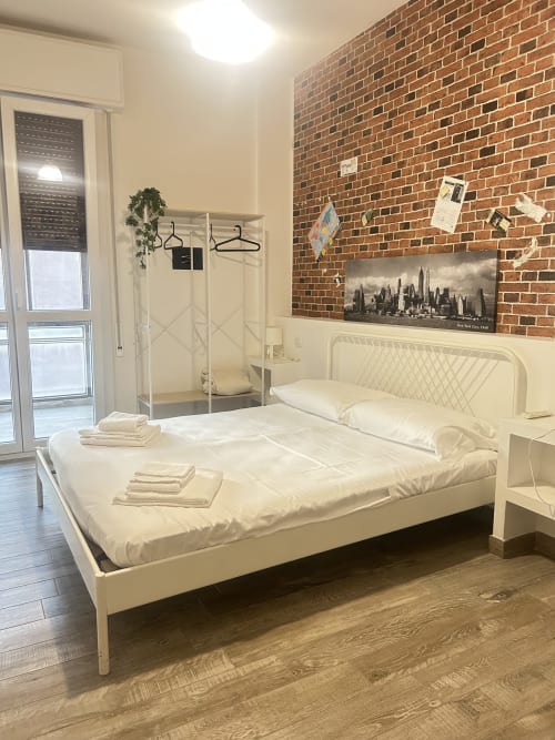Camera luminosa e moderna al B&B Gate 10 di Bologna con letto bianco, muro in laterizio a vista, arte skyline di New York e doccia in vetro