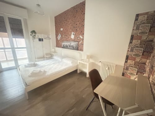 Camera moderna al B&B Gate 10 Fiera Bologna con letto bianco, scrivania, parete in mattoni e accesso al balcone a Bologna, Italia