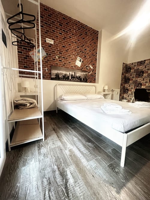 Camera moderna a B&B GATE 10 di Bologna con letto bianco, muro in mattoni a vista, pavimento in legno scuro e scaffalatura in metallo