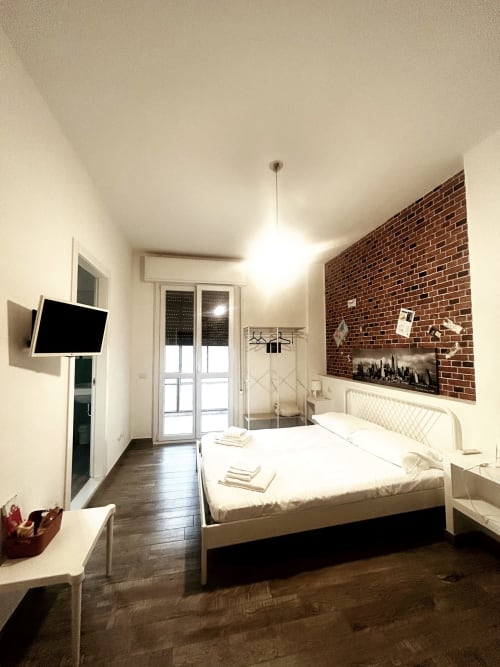 Camera moderna nella B&B Gate 10 di Bologna con letto bianco, parete in laterizio, TV a schermo piatto e porte in vetro sulla terrazza