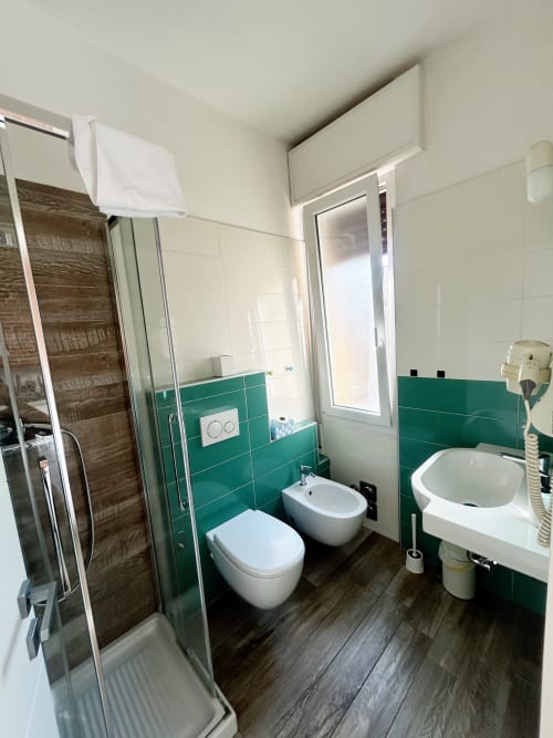 Bagno moderno con parete in piastrelle verdi, wc e bidet bianchi, lavandino e doccia con box in vetro presso B&B Gate 10 Fiera Bologna