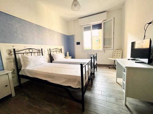 Camera moderna presso B&B GATE 10 Fiera Bologna con letti gemelli, parete blu, scrivania e finestra con vista su Bologna