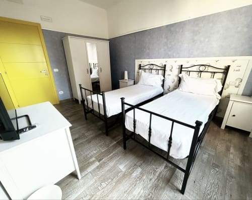 Camera moderna con letti gemelli in metallo nero, porta gialla e parete grigia presso B&B Gate 10 Fiera Bologna
