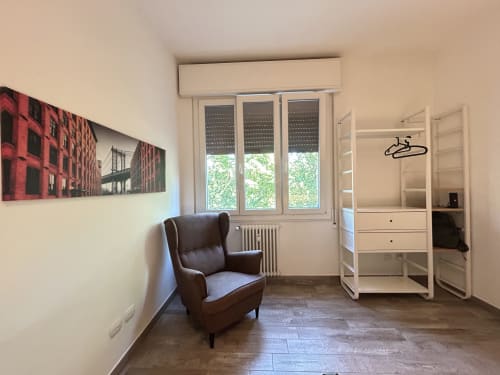 Camera moderna del B&B Gate 10 Fiera Bologna con poltrona marrone, guardaroba bianco e opere d'arte urbana