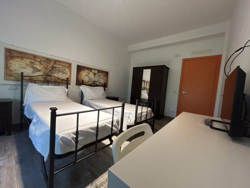 Camera doppia con letti in metallo al B&B Gate 10 Fiera Bologna, con porta in terracotta e quadri con mappe