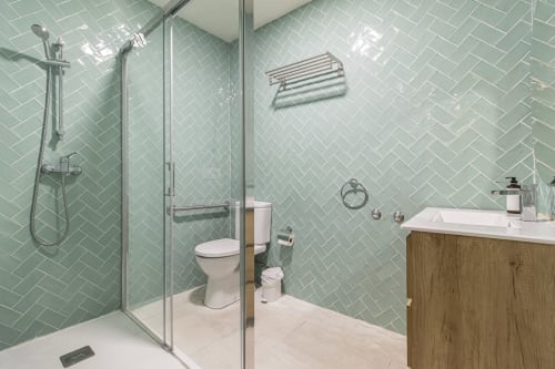 Modern bathroom with mint green herringbone tile, glass shower enclosure, white sink vanity, and polished fixtures at G&H