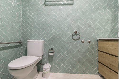 Modern bathroom at G&H Apartments Jerez with mint herringbone tiles, white toilet, wooden vanity, and shower area