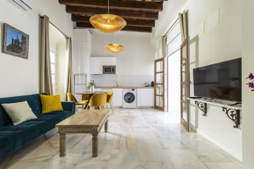 Modern apartment living room with blue sofa, marble floors, kitchen, TV, and golden pendant lights in Jerez de la Frontera