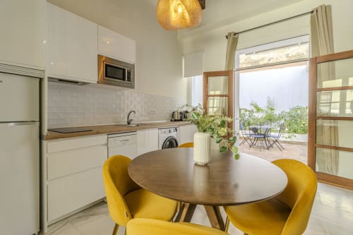 Modern kitchen-dining area at G&H Apartments Jerez with yellow chairs, round table, white cabinets, and garden terrace view