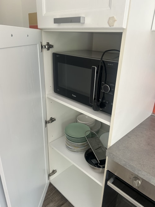 Armadio cucina aperto con microonde, piatti e utensili da cucina presso B&B Gate 10 Fiera Bologna