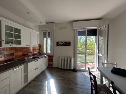 Cucina moderna con mobili bianchi, schienale rosso, pavimenti scuri e porte in vetro che si aprono sul balcone di B&B Gate 10 Fiera