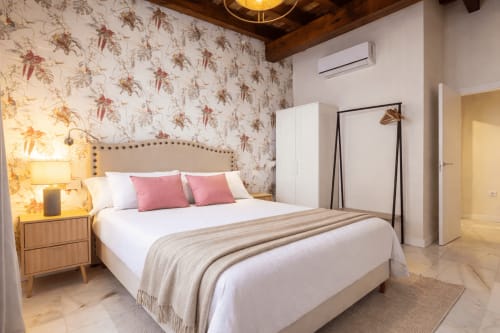 Elegant bedroom at G&H Apartments Jerez with upholstered headboard, pink accents, patterned wallpaper, and modern amenities