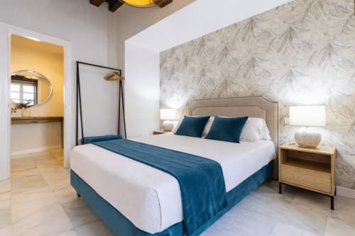 Modern bedroom at G&H Apartments Jerez with queen bed, blue accents, ensuite bathroom, and patterned wallpaper
