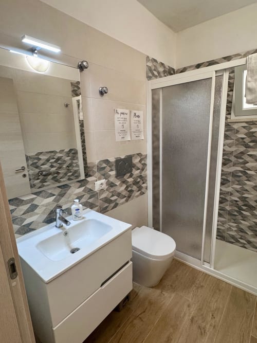 Modern bathroom with geometric tile accents, white sink, toilet, and glass shower enclosure at Casa Vacanze La Coccinella,