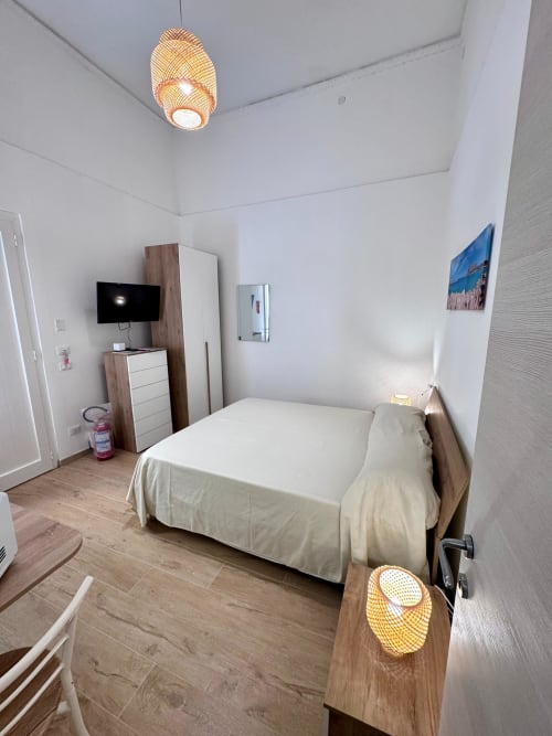 Modern bedroom in Casa Vacanze La Coccinella, Trapani with bed, TV, wooden furniture and woven pendant lights