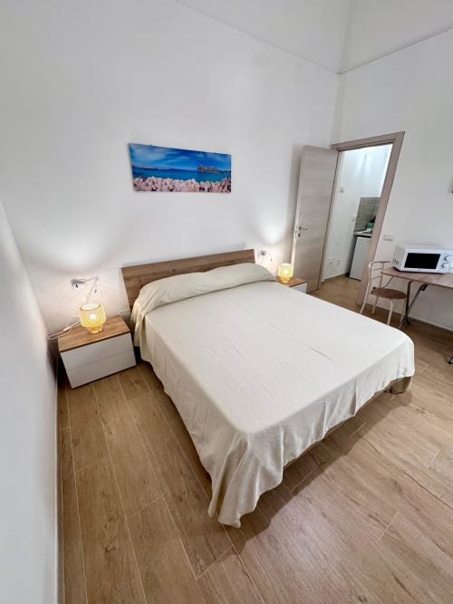 Bright bedroom with queen bed, wooden nightstands, and coastal artwork at Casa Vacanze La Coccinella in Trapani, Italy
