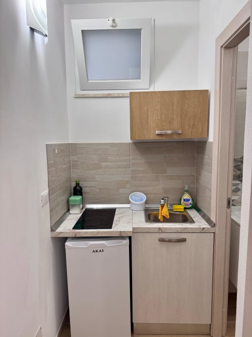 Compact kitchenette with sink, cooktop, refrigerator, and wooden cabinets in Casa Vacanze La Coccinella apartment, Trapani