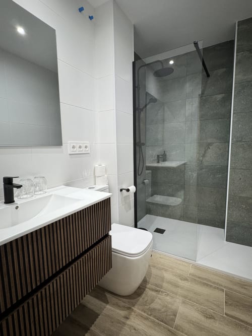 Bany modern a l'Hotel Oreneta de Gironella amb vanitat negra, lavabo blanc, inodor i dutxa tipus italiana amb rajoles grises