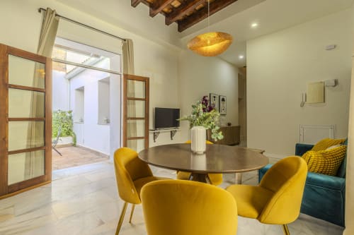 Modern dining area in G&H Apartments Jerez de la Frontera with yellow chairs, round table, and garden view doors