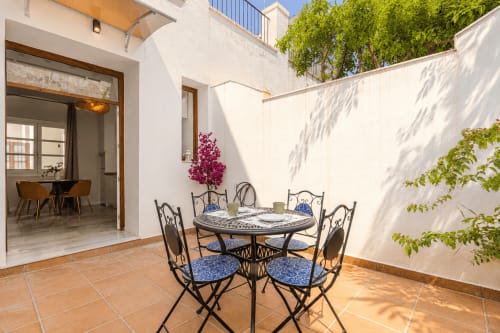 Sunny garden terrace at G&H Apartments Jerez with wrought iron dining table, blue cushioned chairs, and magenta flowers in