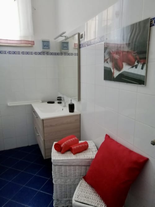Modern bathroom with white tiles, wooden sink vanity, red accents, and wicker storage baskets at I colori della Sicilia,