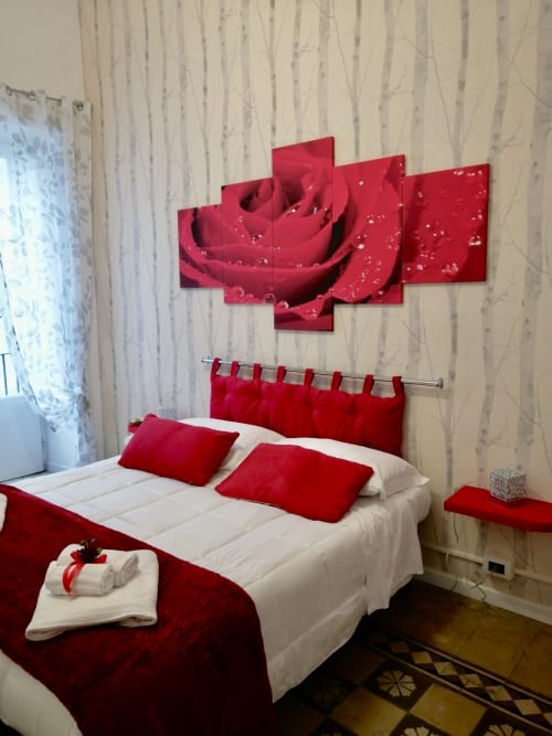Camera Rosa presso I colori della Sicilia a Caltagirone, arredata in rosso e bianco con opere d'arte floreale e una confortevole biancheria da letto