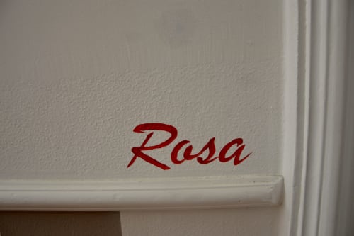 Red "Rosa" room name written on white wall at I colori della Sicilia boutique hotel in Caltagirone, Sicily