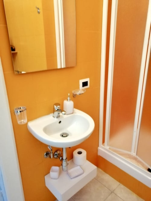 Bright orange bathroom with white pedestal sink, mirror, and modern amenities at I colori della Sicilia hotel in Caltagirone,