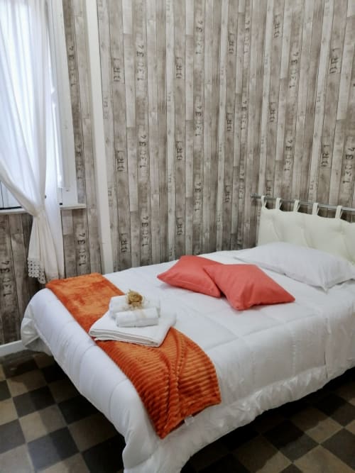 Camera accogliente all'I colori della Sicilia di Caltagirone con biancheria bianca, cuscini corallo, plaid arancioni e rivestimenti in legno
