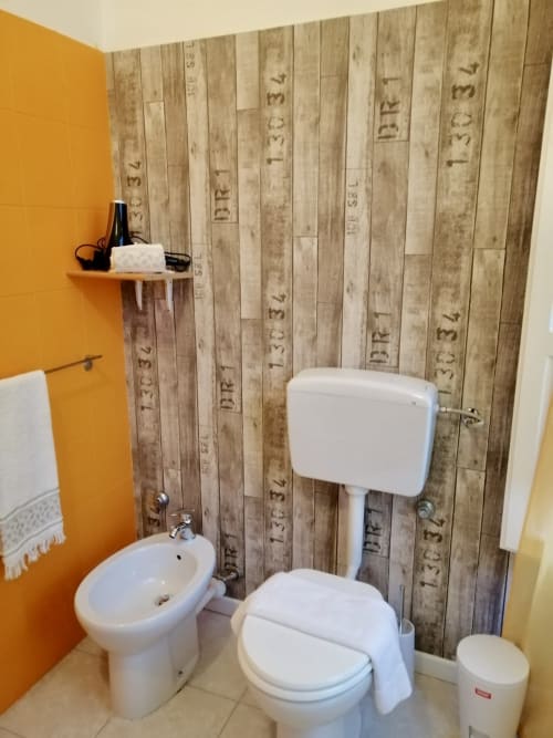 Modern bathroom at I colori della Sicilia in Caltagirone with rustic wood-patterned tiles, white fixtures, and bright yellow