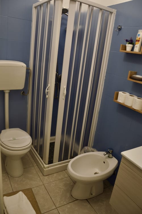 Modern bathroom with blue tile walls, white toilet and bidet, striped shower stall at Lavanda room in Caltagirone B&B