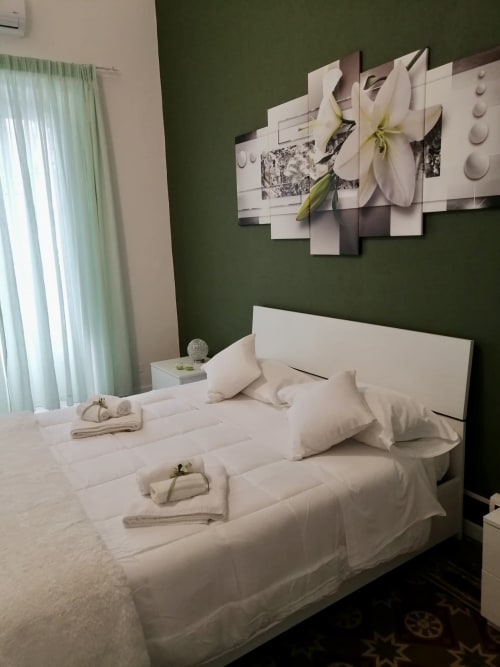 Camera da letto presso I colori della Sicilia a Caltagirone con biancheria bianca, parete verde accento e opere d'arte floreale