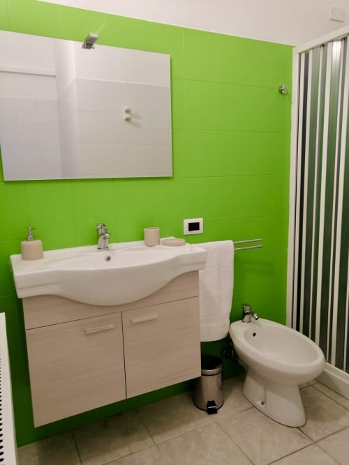 Modern bathroom at I colori della Sicilia with bright lime green walls, curved white sink, wooden vanity, bidet, and striped