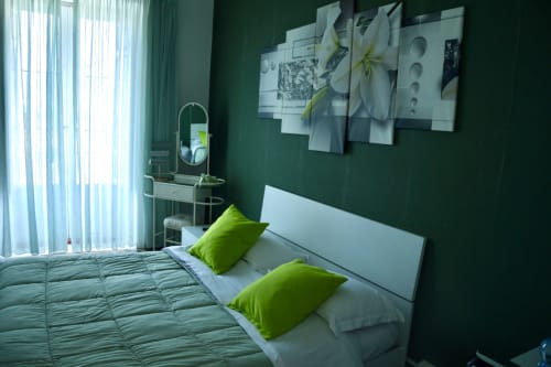 Modern bedroom with green walls, white bed, lime pillows, wall art, and mirror at Giglio room in Caltagirone, Sicily
