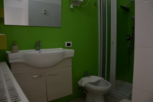 Modern bathroom with bright green walls, white sink with vanity, toilet, and shower enclosure at I colori della Sicilia hotel