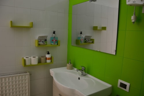 Modern bathroom with green accents, white sink, mirror, and yellow shelving with toiletries at I colori della Sicilia,