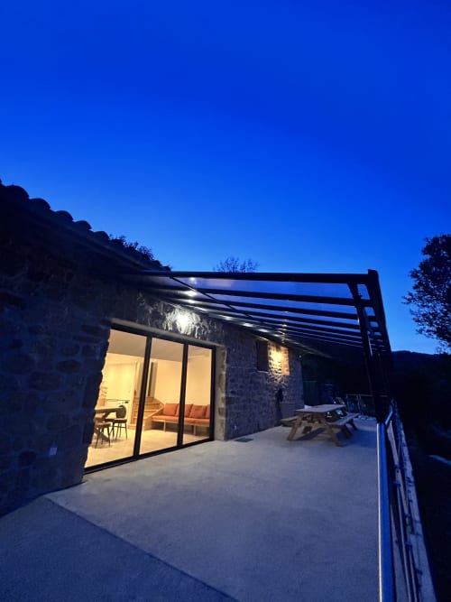 Gîte Les Oliviers d'Ardèche at dusk with illuminated patio, stone walls, and mountain views in Chalencon