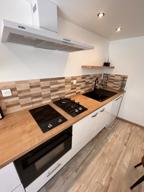Modern kitchen in Gîte Les Oliviers d'Ardèche cottage with wooden countertop, gas cooktop, black sink, and geometric tile