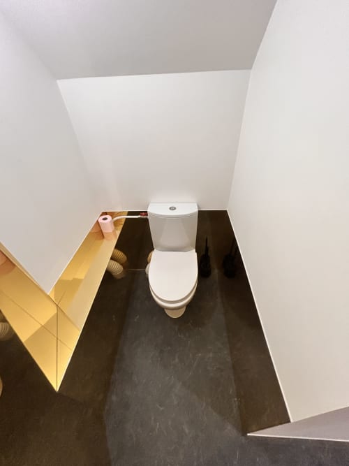 Modern toilet in white bathroom with dark floor and golden wall paneling at Gîte Les Oliviers d'Ardèche, Chalencon, France