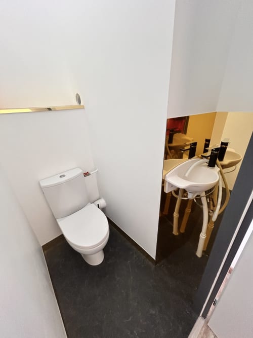 Modern bathroom in Gîte Les Oliviers d'Ardèche cottage with white toilet, vanity sink, and dark tile flooring