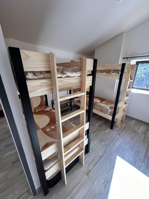 Bright dormitory room with wooden bunk beds featuring black metal frames and beige bedding in Gîte Les Oliviers d'Ardèche