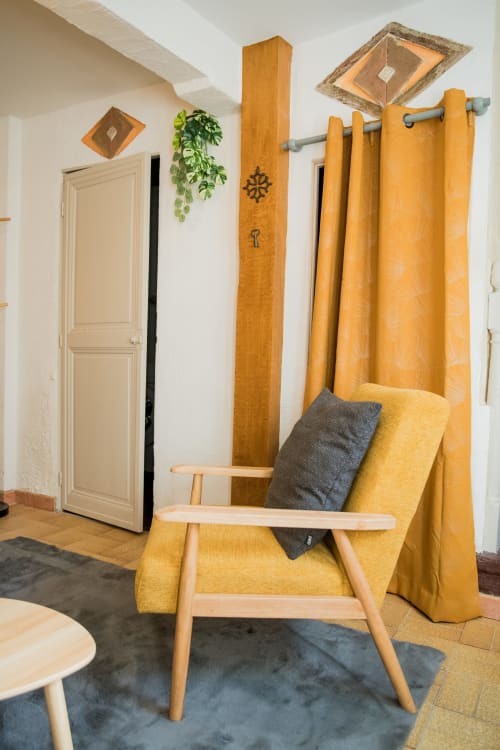 Fauteuil jaune moutarde aux accoudoirs en bois dans le salon chaleureux de Mi Casa Es Su Casa, Carcassonne