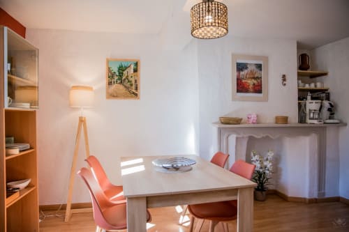 Séjour lumineux du cottage La Petite Vue à Carcassonne avec table beige, chaises corail, cheminée et tableaux encadrés