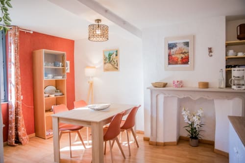 Salle à manger lumineuse au cottage La Petite Vue à Carcassonne, avec mur accent corail, table en bois et foyer.