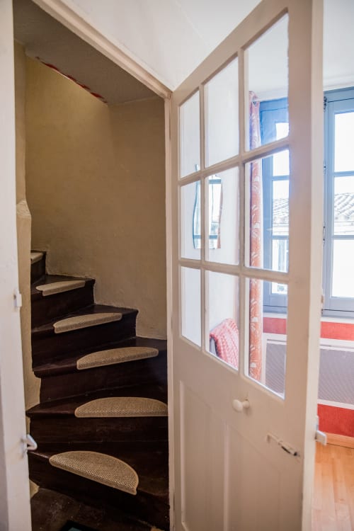 Escalier à moquette beige menant à l'étage supérieur d'un gîte à Carcassonne, avec de grandes fenêtres lumineuses offrant une vue sur un monument emblématique