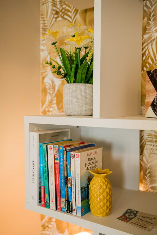 Étagères blanches décorées de marguerites jaunes, livres et ananas dans un cottage de Carcassonne