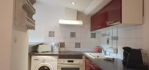 Cuisine moderne dans un appartement de Carcassonne avec armoires bordeaux, appareils blancs et carrelage décoratif